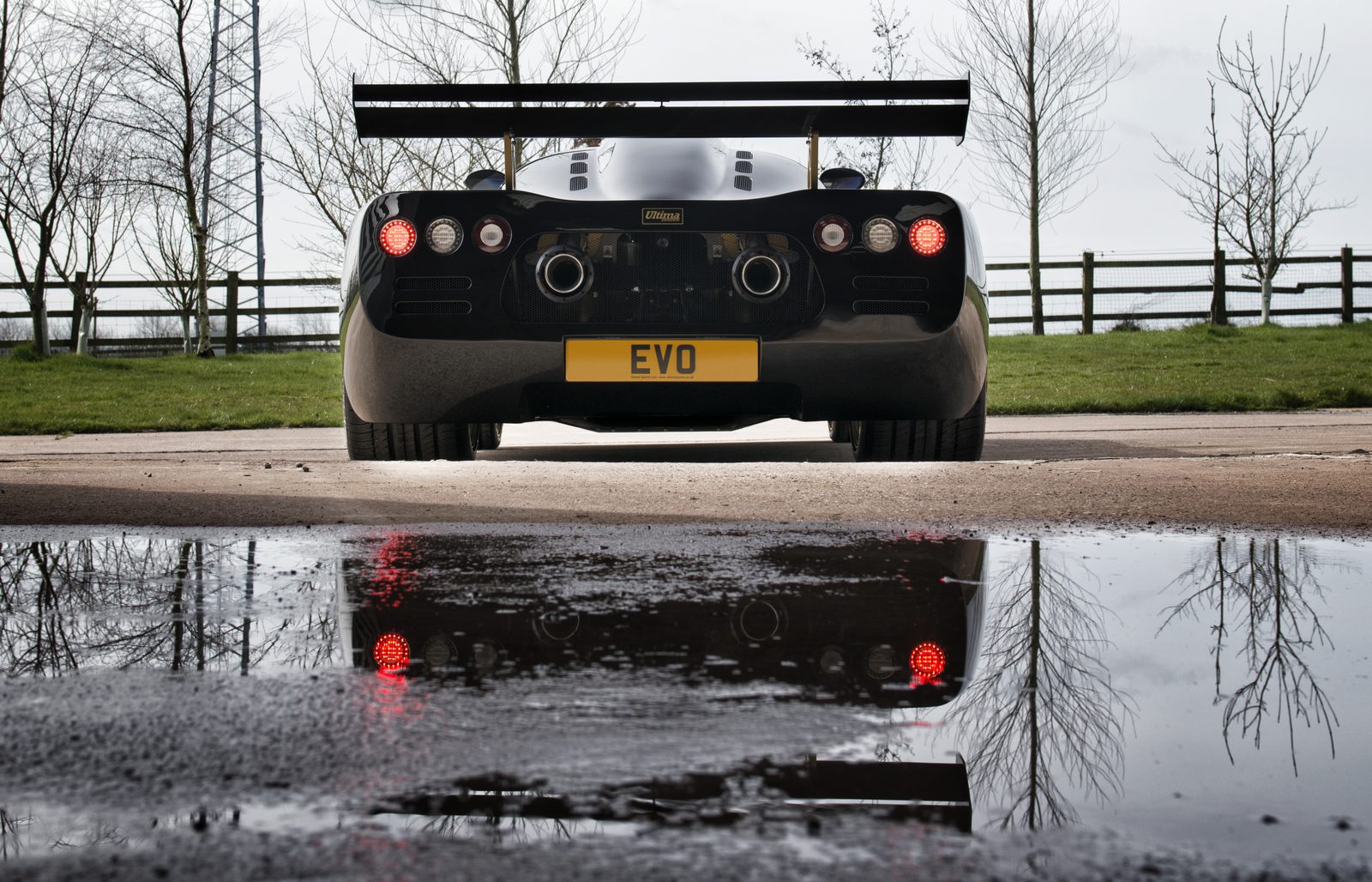Rear view of a black Ultima Evolution Coupe reflected in water