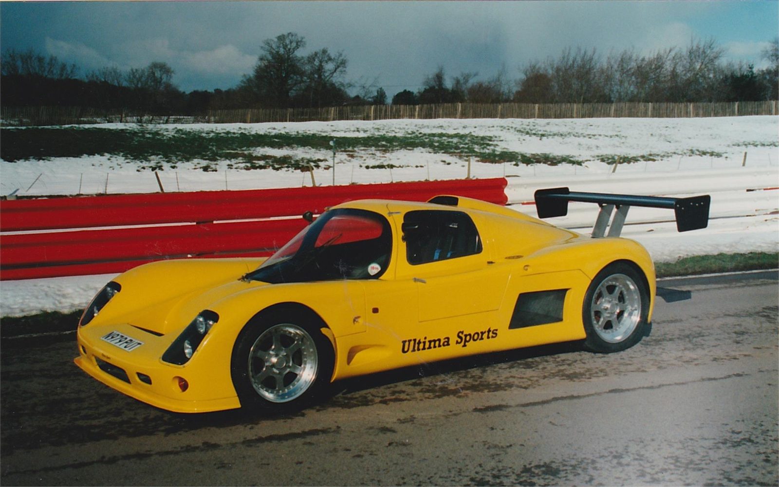 Yellow Ultima Sport in side view at a snowy circuit