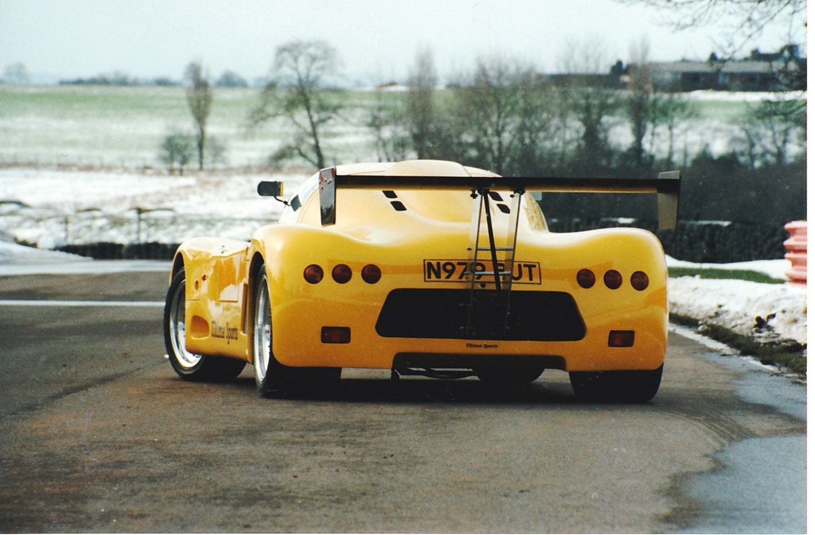 Rear view of a yellow Ultima Sport at a snowy circuit