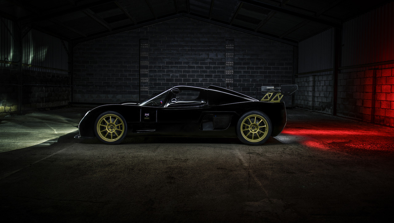 A black Ultima Evolution photographed side-on inside a dark industrial building, with green and red light falling across the walls