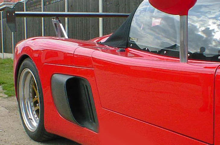 Side view of a red Ultima showing the driver-side intake behind the door.